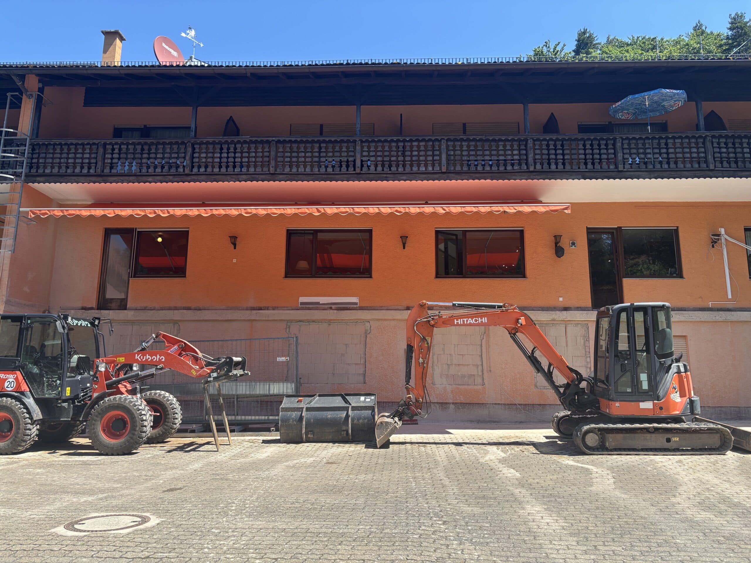 Baufahrzeuge (Kubota Radlader und Hitachi Minibagger) vor der Fassade des Waldhotel Heppe während der Umbauarbeiten