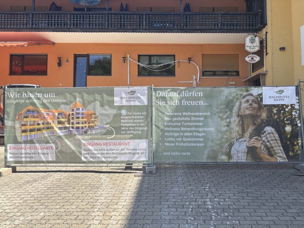 Bauzaun-Banner am Waldhotel Heppe mit Informationen zum Umbau: Eingänge während der Bauphase und Ausblick auf neue Ausstattung wie Panorama-Wellnessbereich, Turmzimmer und Aufzüge