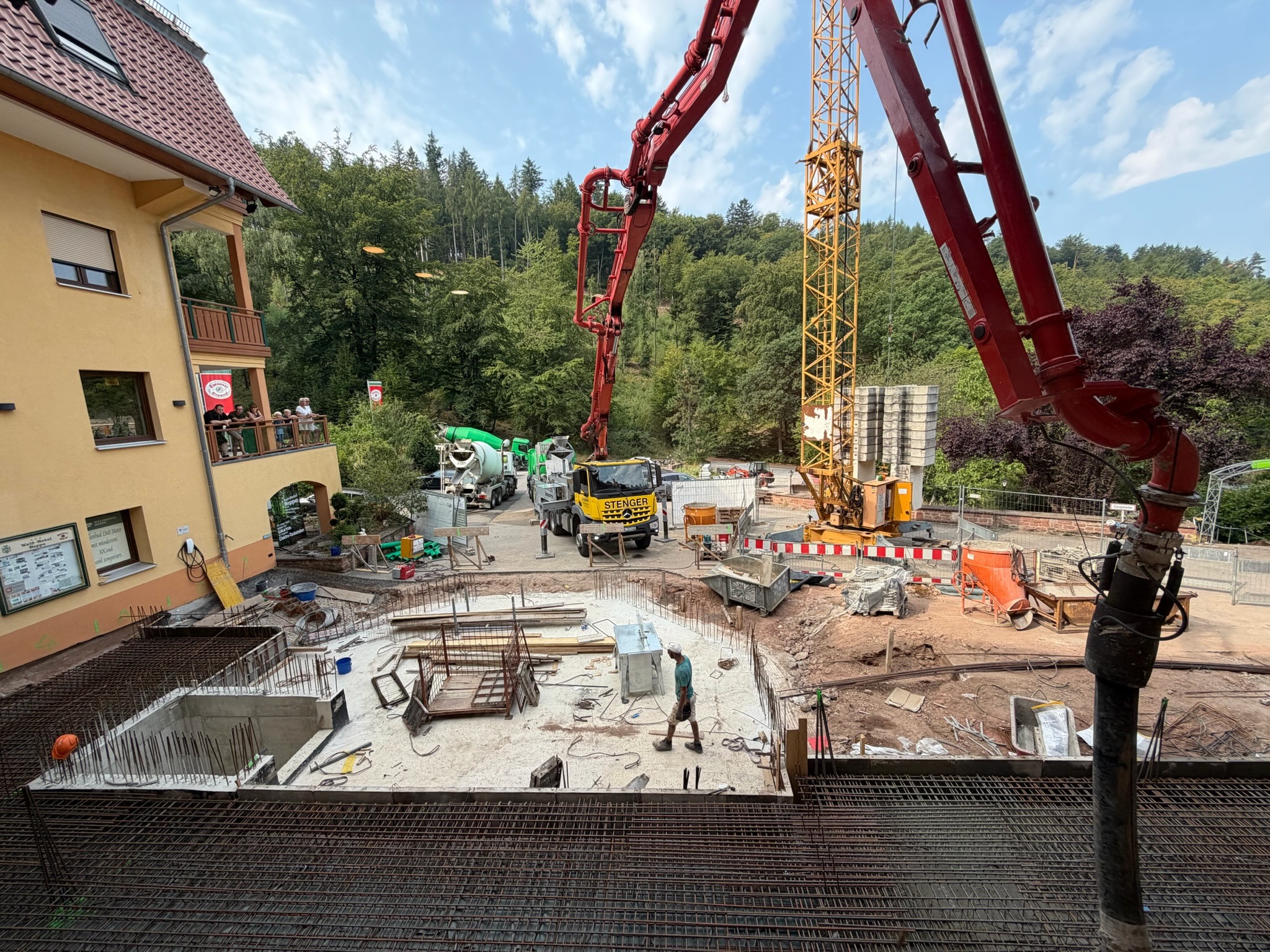Baustelle der Waldhotel-Heppe-Erweiterung mit Betonpumpe, Baukran und Bodenplatte samt Bewehrungsstahl, im Hintergrund Zuschauer auf dem Balkon und der Spessartwald